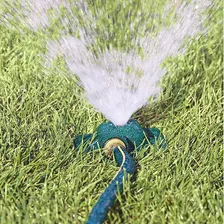 Melnor cast iron square spot sprinkler sitting low in cut grass with a garden hose attached, throwing a fine fan of water upward from its centre