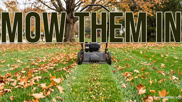 A walk-behind mower crossing a green lawn strewn with fallen orange and brown leaves under a large tree, a clearer strip of grass with only shredded fragments in front of its deck, with the words “Mow Them In” set across the top