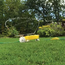 Nelson Rain Train yellow cast iron traveling sprinkler on a lawn spraying from its rotating arm, following the green garden hose laid out ahead of it with the shut-off ramp visible on the hose