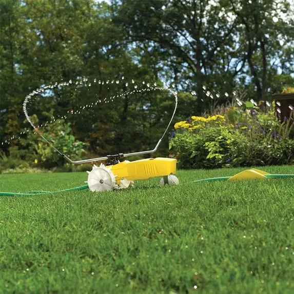 Nelson Rain Train yellow cast iron traveling sprinkler on a lawn spraying from its rotating arm, following the green garden hose laid out ahead of it with the shut-off ramp visible on the hose